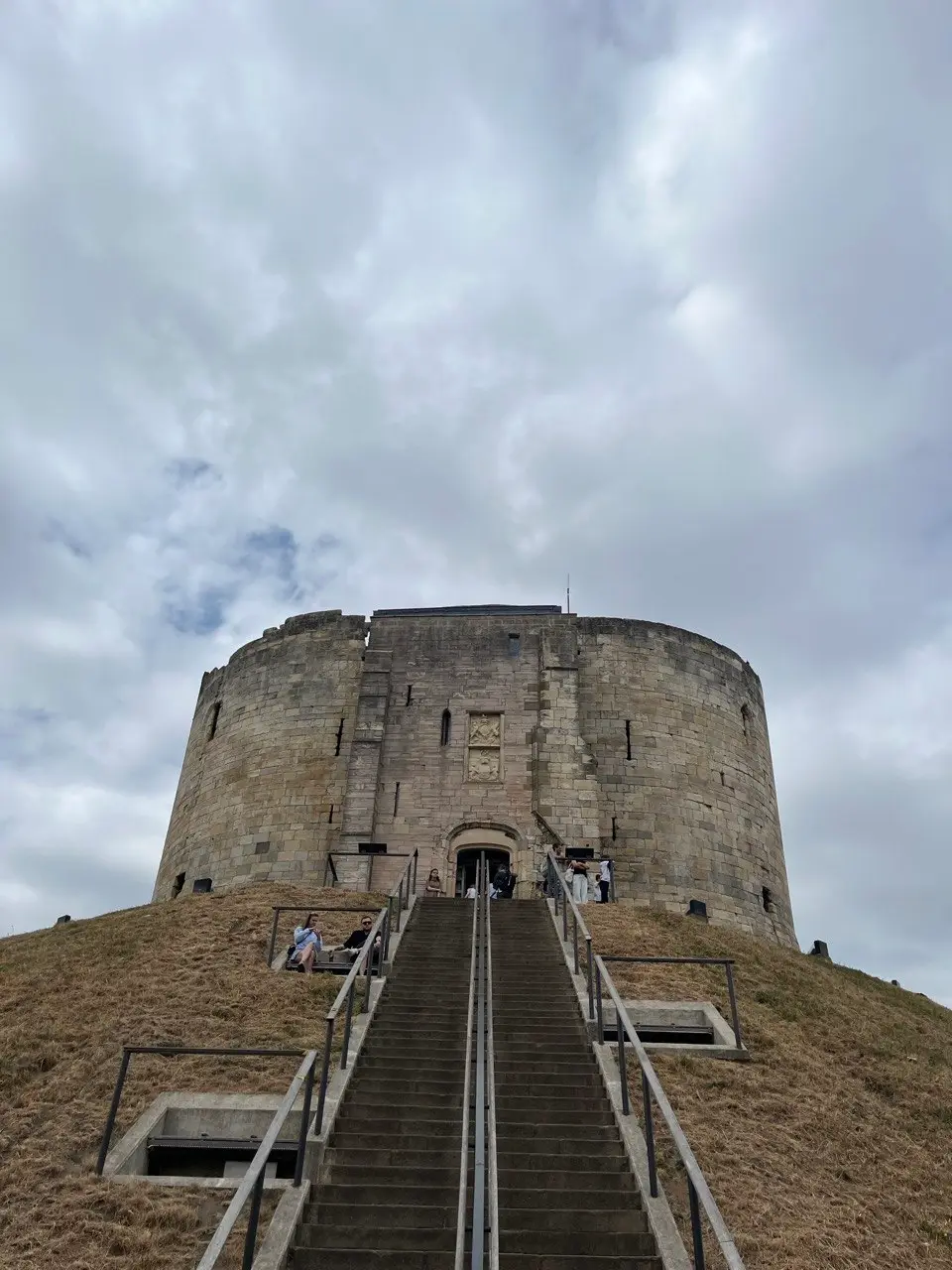 Clifford's Tower, a squat round stone keep on top of a grass mound, with a long flight of steps leading up to its entrance